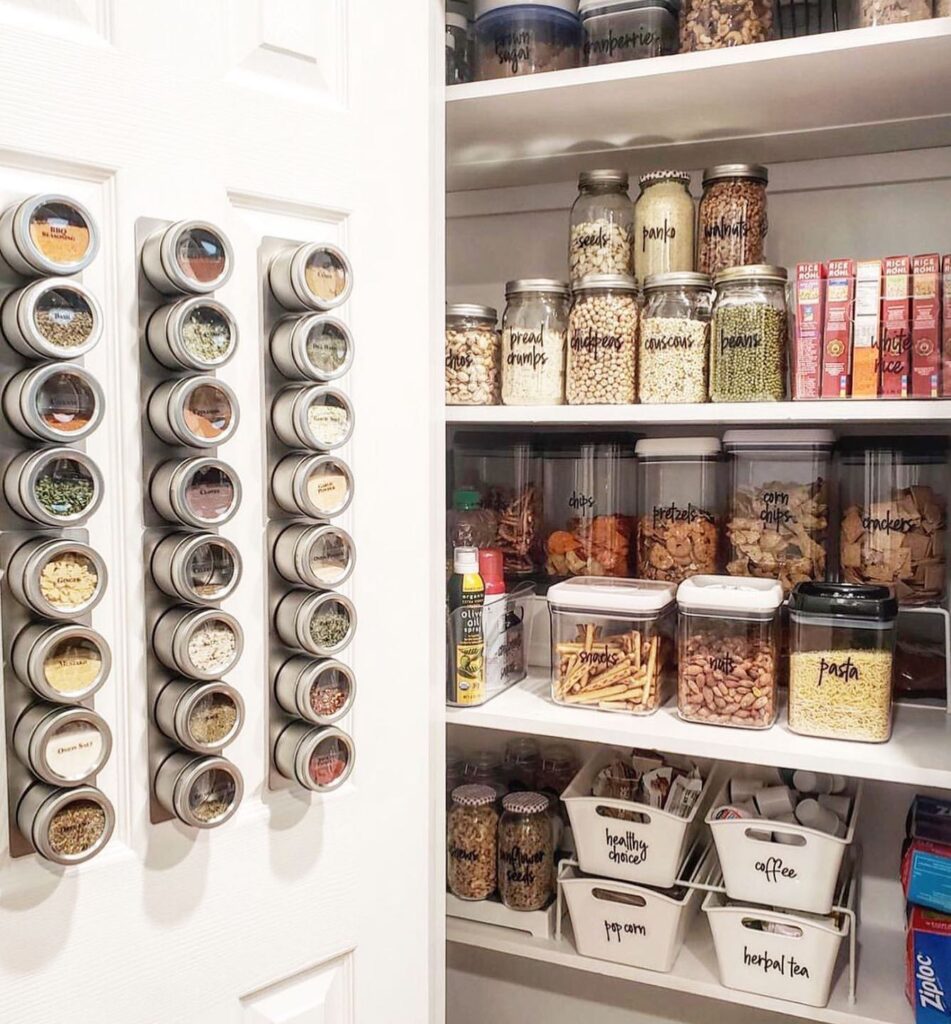 Small pantry door fitted with slim wooden spice racks filled with neatly arranged spice jars, cozy warm lighting reflecting on glass jars, soft neutral kitchen tones, white pantry shelves visible in background, Pinterest-worthy organized kitchen storage with modern farmhouse style and natural wood textures.