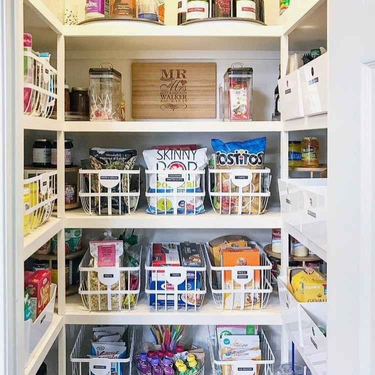 Small pantry shelf styled with labeled snack baskets filled with granola bars, crackers, fruit snacks, and chips, cozy family kitchen design with warm lighting, white shelves and woven storage bins, Pinterest-style organized snack station with inviting textures and natural daylight.