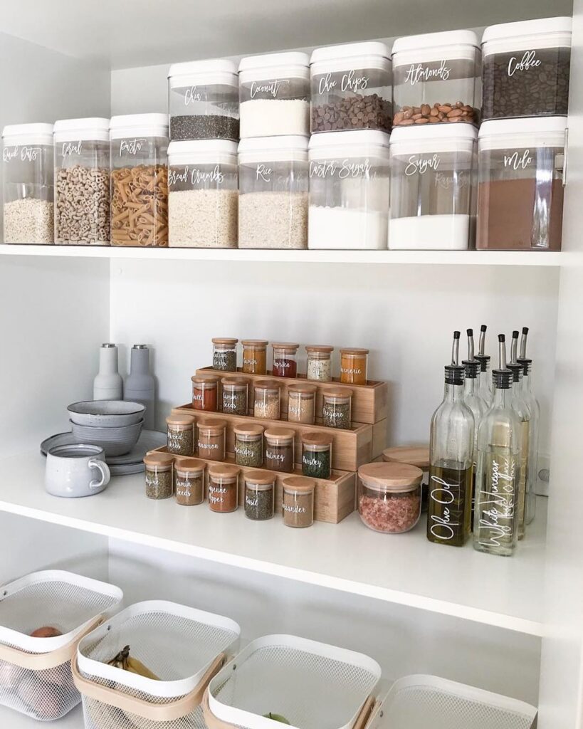 Small pantry shelf with tiered wooden organizers holding rows of soup cans, spice jars, and small food tins arranged neatly in stepped levels, cozy kitchen lighting with warm white LED shelf lights, white painted shelving with neutral pantry jars, woven storage baskets nearby, minimalist Pinterest-style kitchen storage scene with natural textures and soft shadows.
