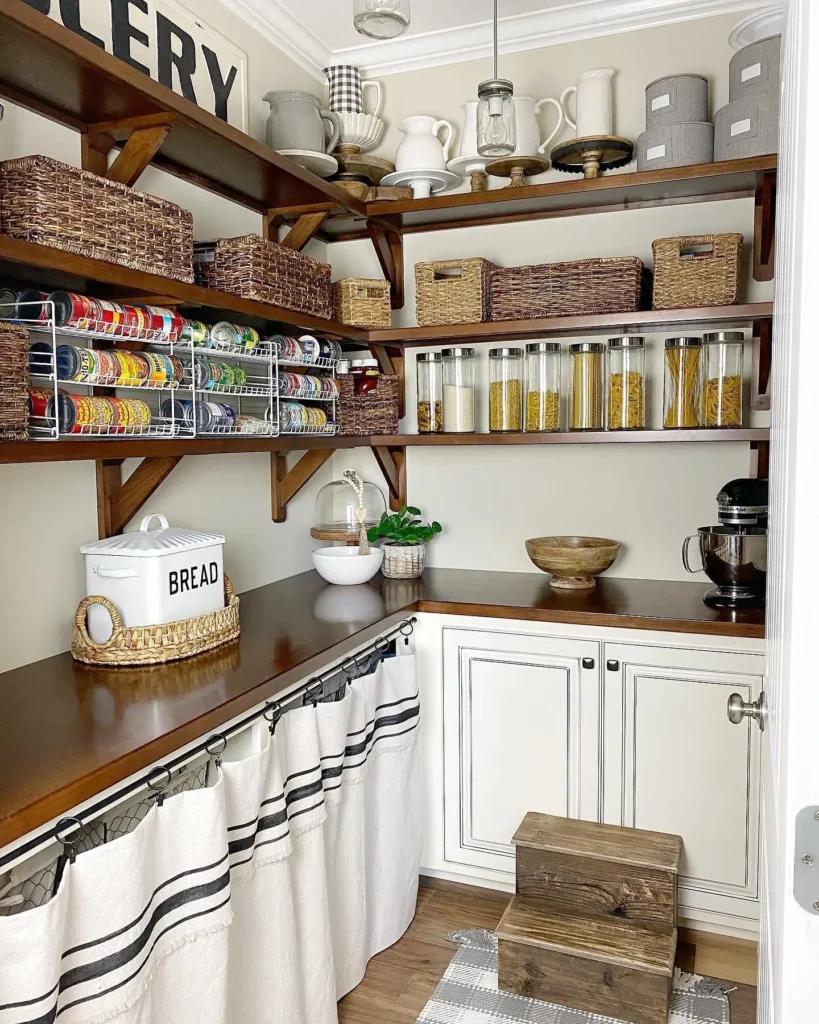 Cozy pantry shelves styled with woven rattan baskets labeled snacks, baking supplies, and breakfast items, neutral farmhouse kitchen design with soft beige tones, white shelves, natural wood textures, linen kitchen towels hanging nearby, gentle window light creating warm cozy shadows, Pinterest-style organized pantry scene.